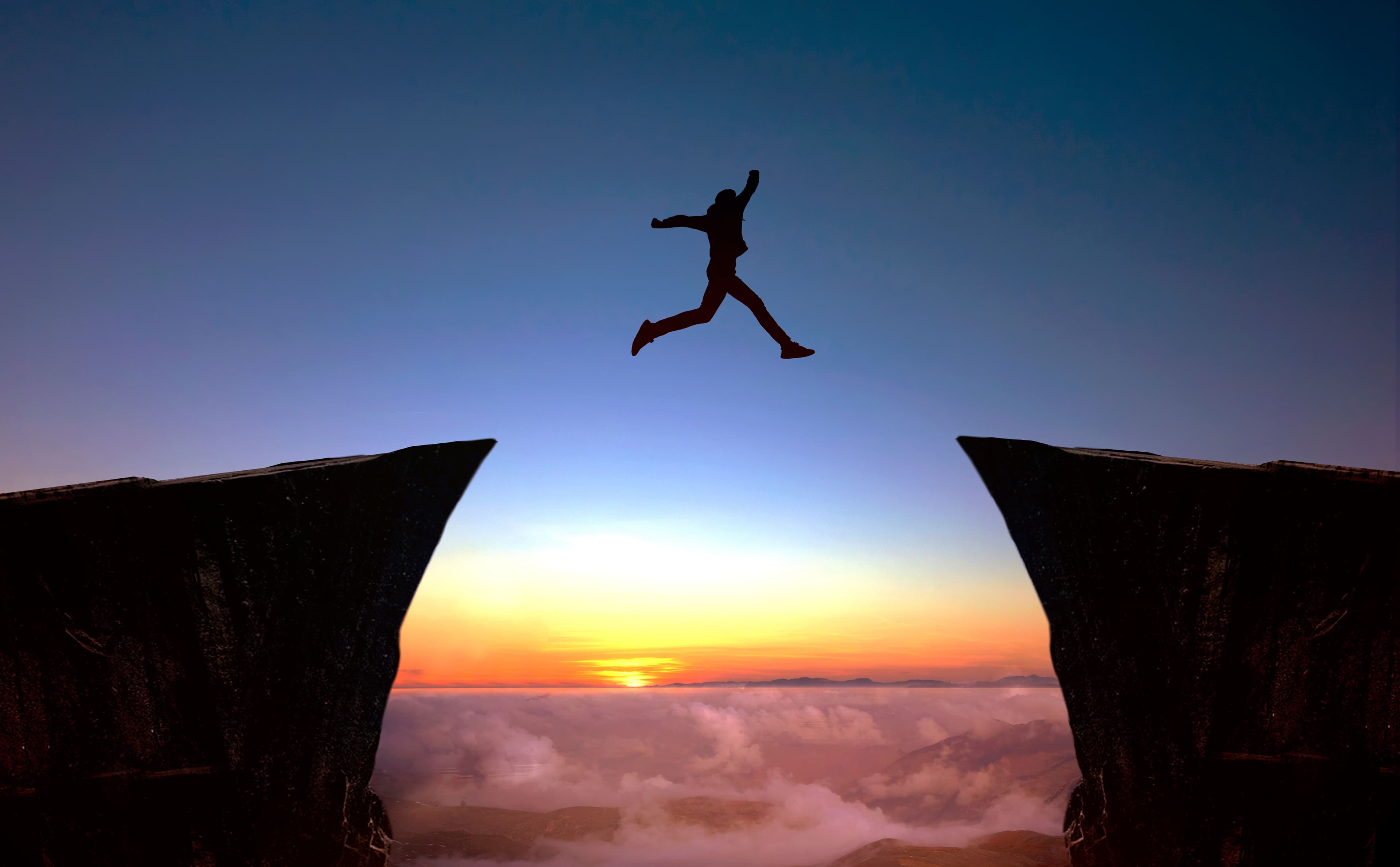 man jumping from one cliff to another