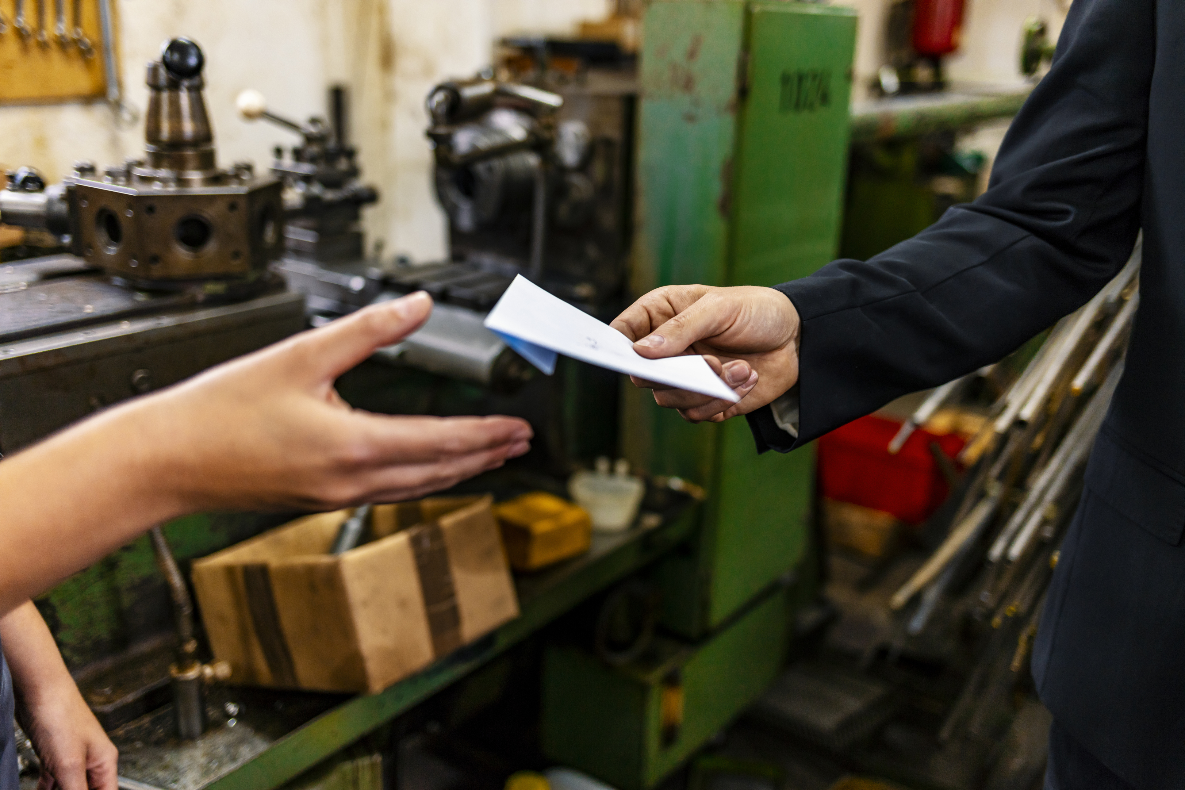 Human hand handing over a paper sheet to the other human hand in garage or factory type of environment.