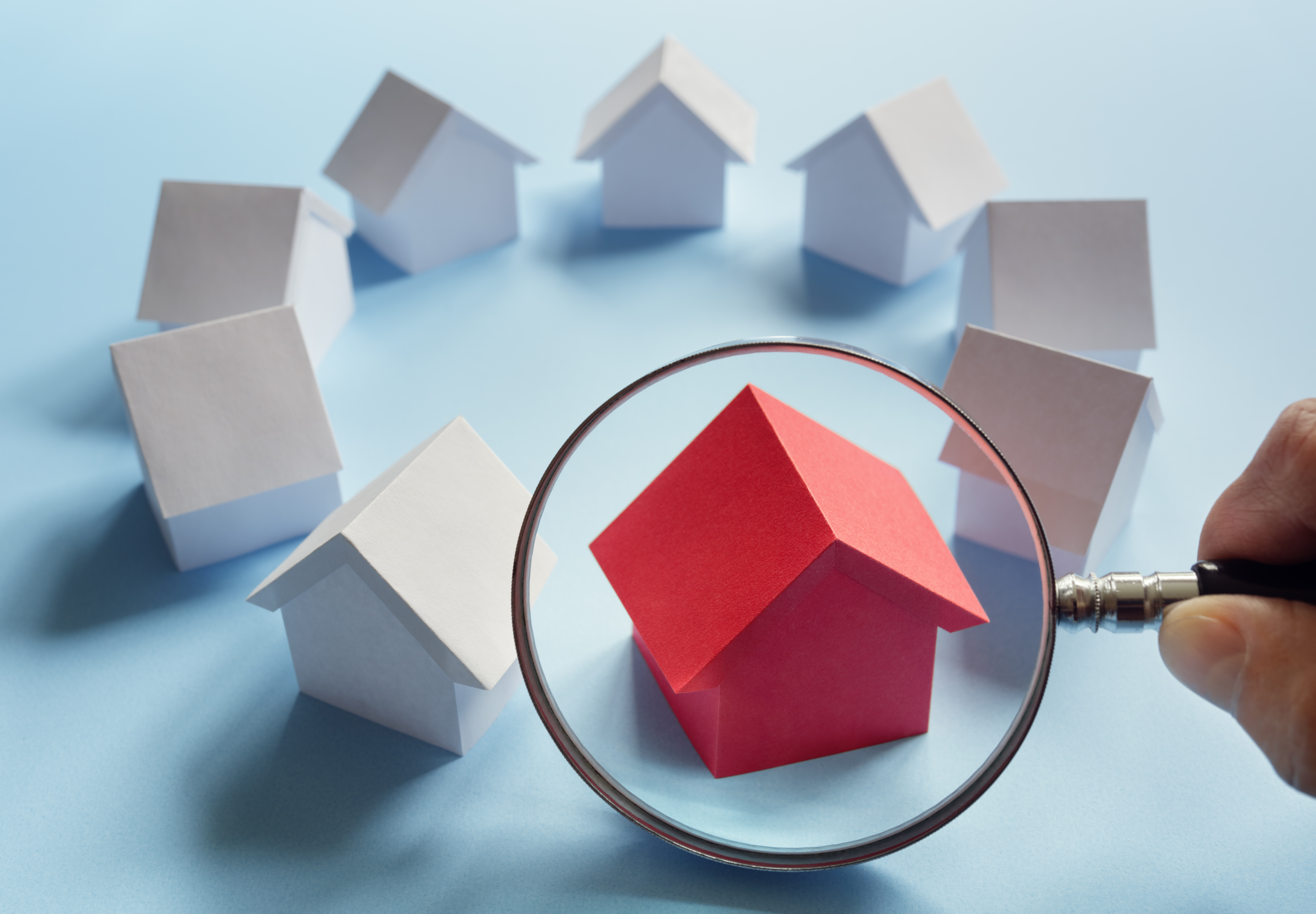 Magnifying glass focuusing on the miniature of red house among other white miniatrure houses arranged in circle - Housing Observatory Informs Policy for Over Two Decades - hero image