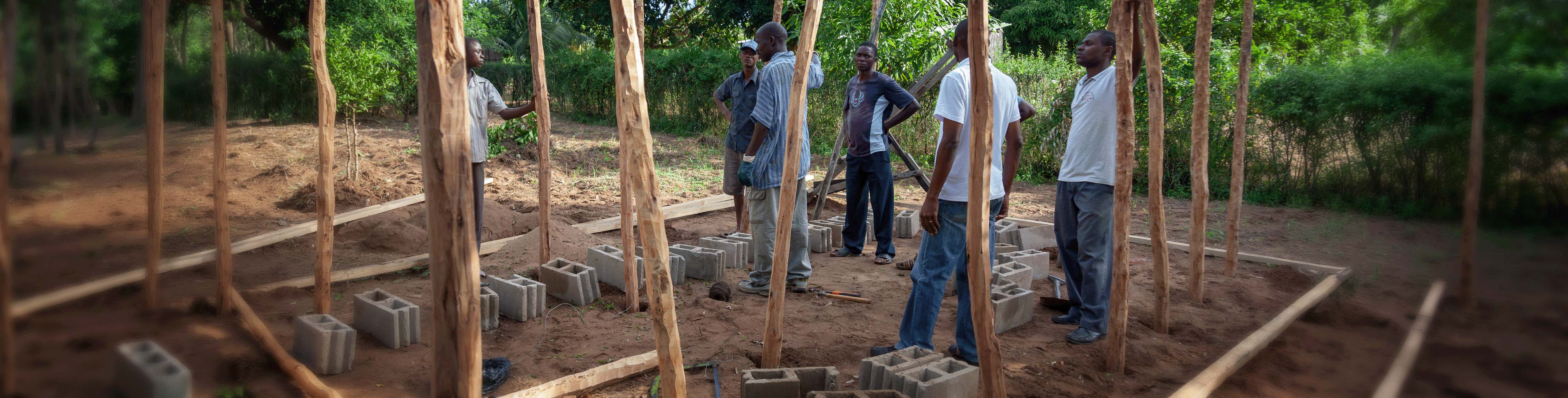 A group of people discussing at an outdoor construction site with wooden posts and cinder blocks aligned on the ground
