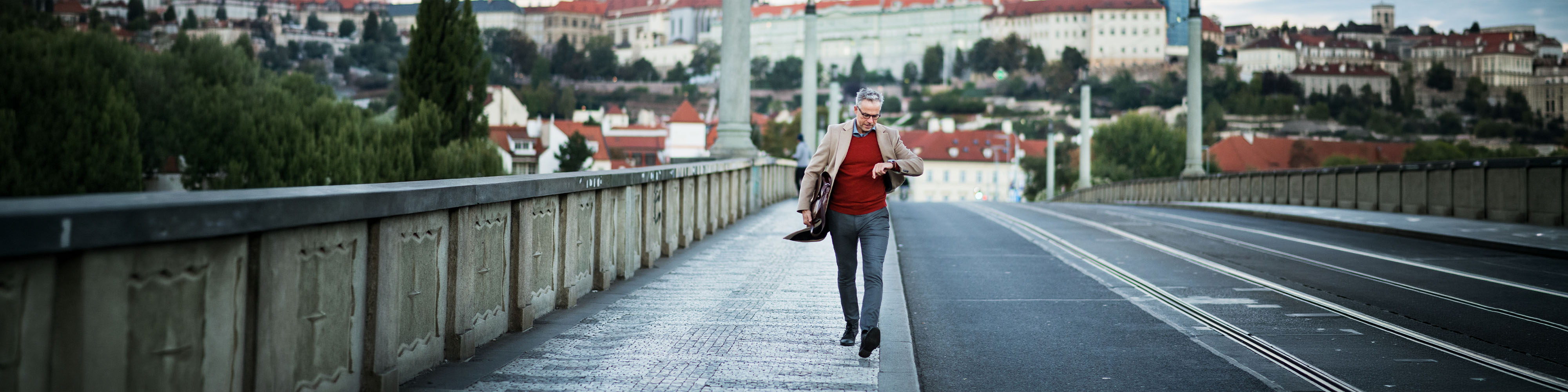 Business man rushing through the bridge in Prague city looking at his wrist watch.
